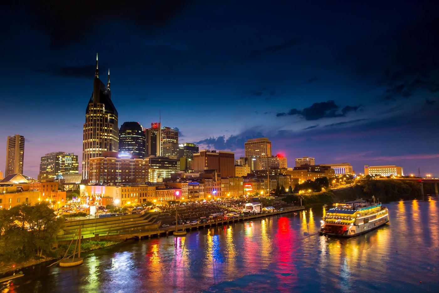 The Nashville, Tennessee riverfront at night along Broadway and the Cumberland River, with a river cruise boat passing the entertainment district
